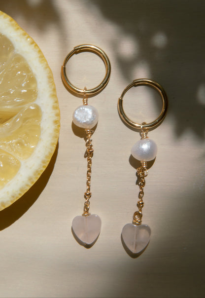 Gold earrings with pearl and heart-shaped charms on a light background