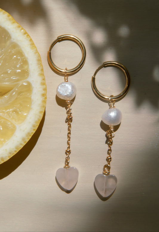 Gold earrings with pearl and heart-shaped charms on a light background