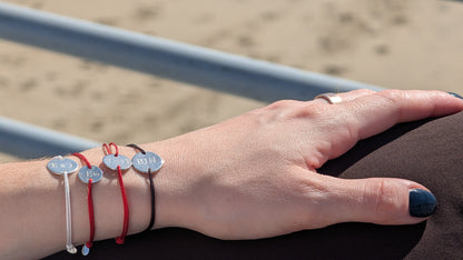 Hand wearing multiple bracelets with heart-shaped charms on a blurred beach background